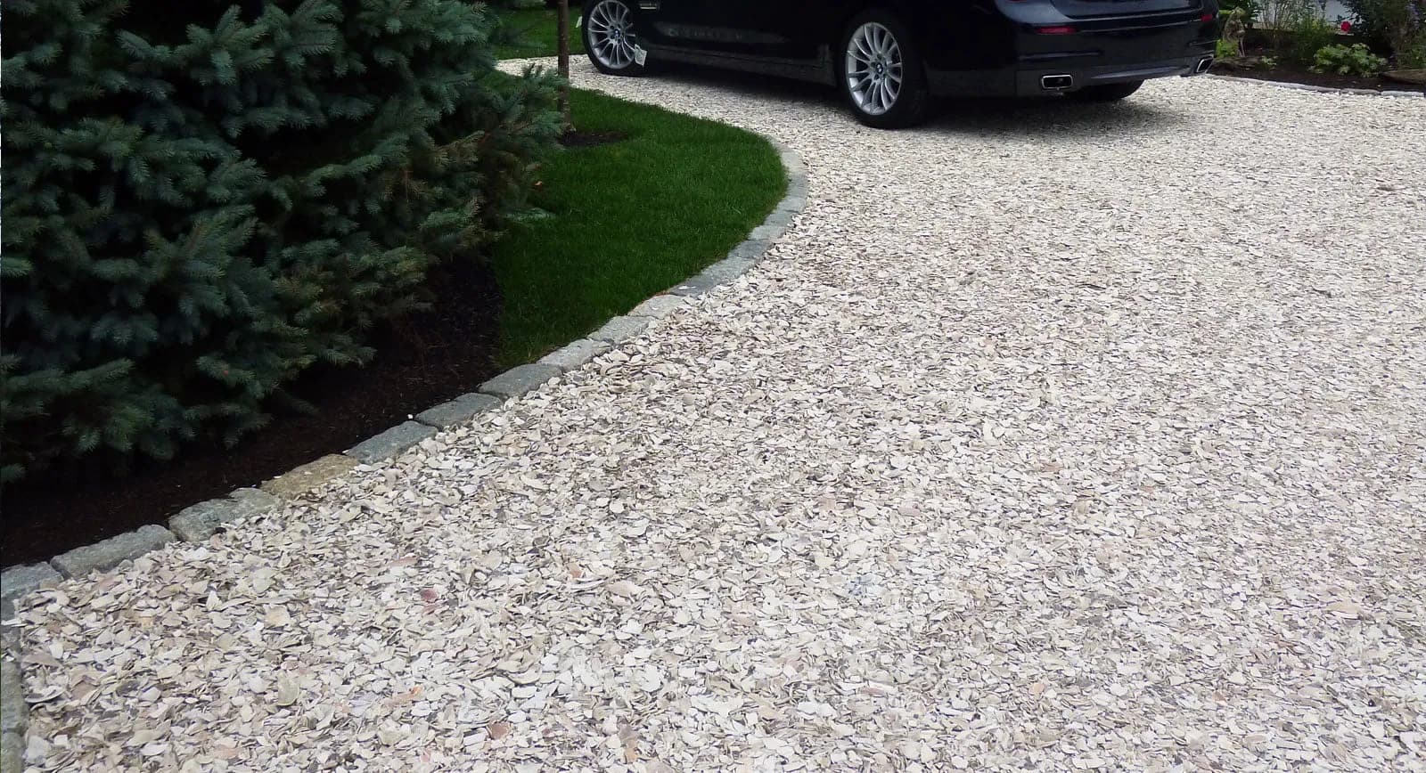 A crushed shell driveway edged with granite cobbles against a lawn